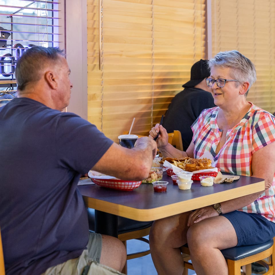 Two diners enjoy fried seafood, fries, salad, and dipping sauces at a restaurant table.