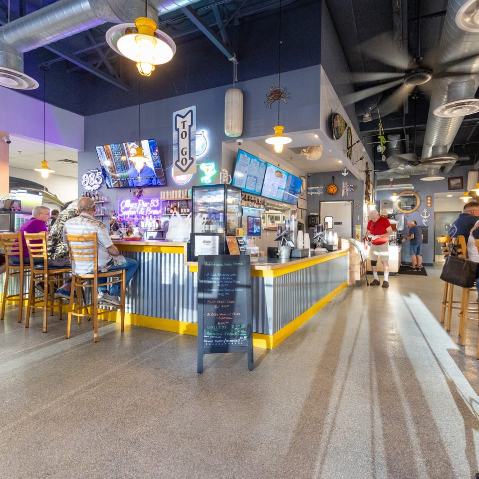 Busy seafood restaurant interior with nautical décor, exposed ducts, bar counter, digital menus, and diners seated at tables.