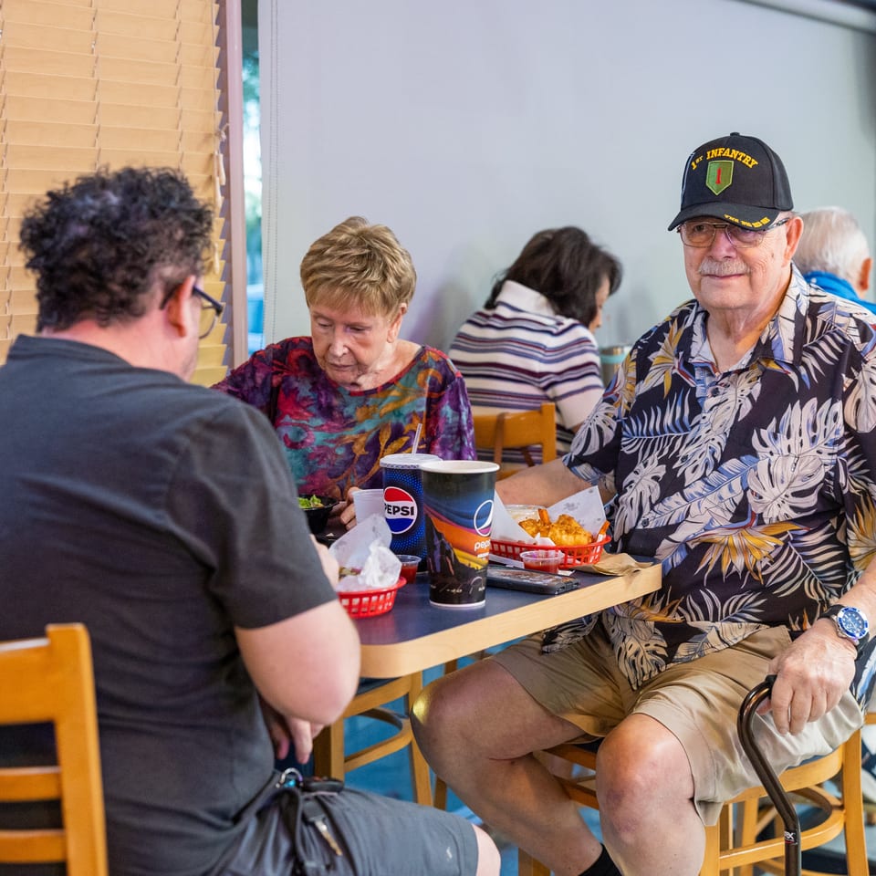 Friends enjoy a casual restaurant meal together, with fried food, drinks, and several diners seated around a table.