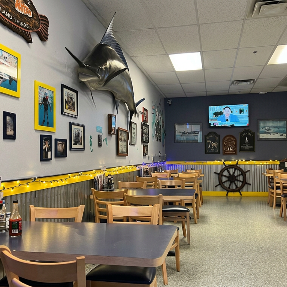 Nautical-themed restaurant dining room with wooden tables, maritime decor, mounted fish, framed photos, and one seated patron.